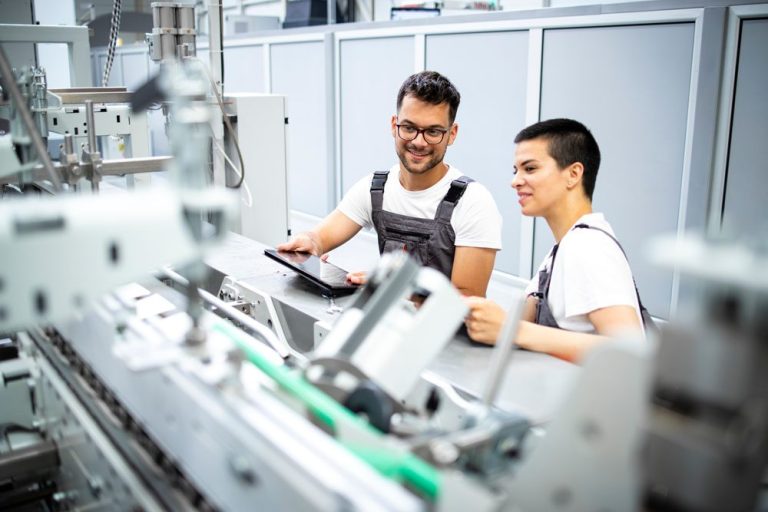 Zwei Personen in Arbeitskleidung beobachten eine Maschine in einem Unternehmen in der Industrie.