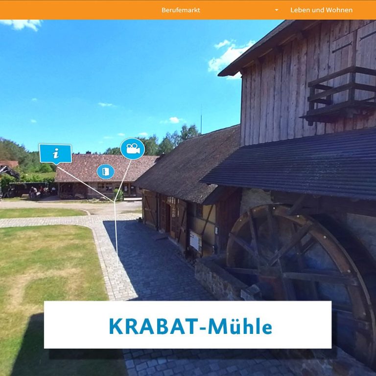 Die KRABAT-Mühle mit Wasserrad und historischen Gebäuden in ländlicher Umgebung.